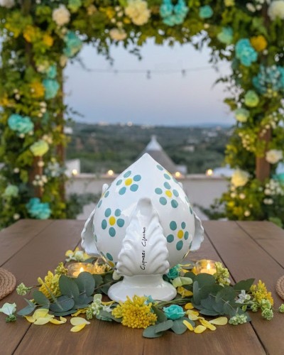 Pumo Poz Studio fiori verde Tiffany e firma Claudio Capozzi su sfondo trulli pugliesi al tramonto.