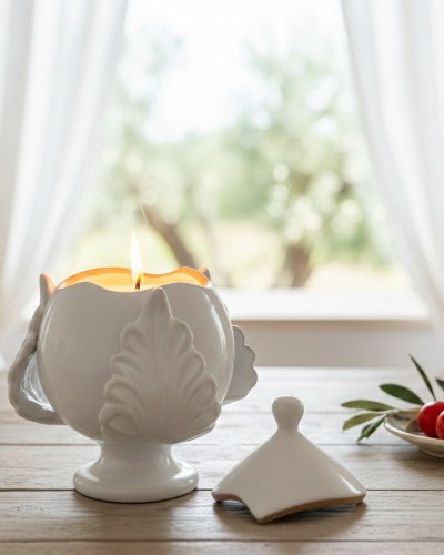 Pumo pugliese Poz Studio aperto con candela accesa e coperchio su tavolo in legno, con pomodori, olive e sfondo di uliveti.